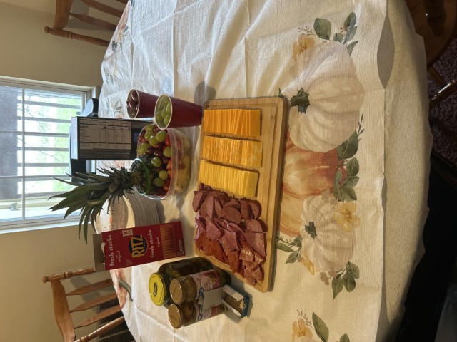 A platter of cheeses, meats, and crackers on a wooden cutting board.